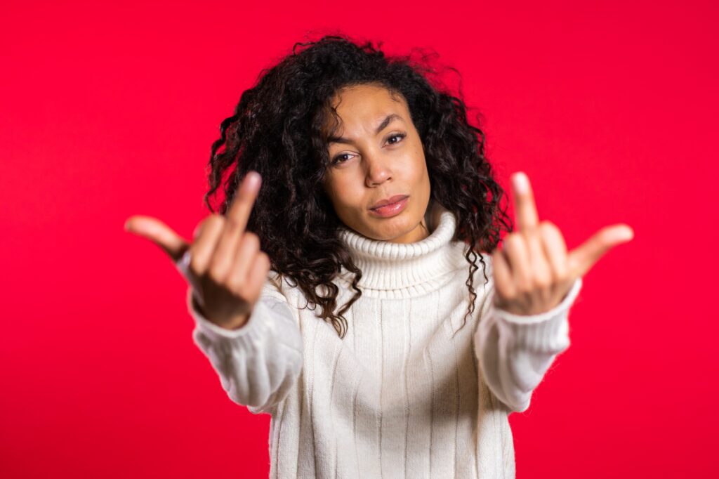 Young woman with african hair on red background showing middle finger - gesture of fuck.